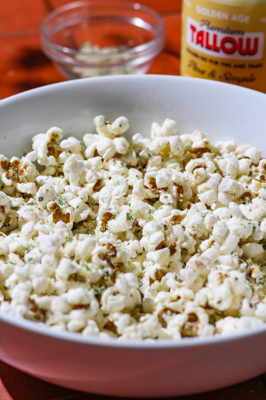 A large bowl filled with Garlic Herb Tallow Popcorn popped in Golden Age Fats Beef Tallow, garnished with fresh herbs and shredded cheese.