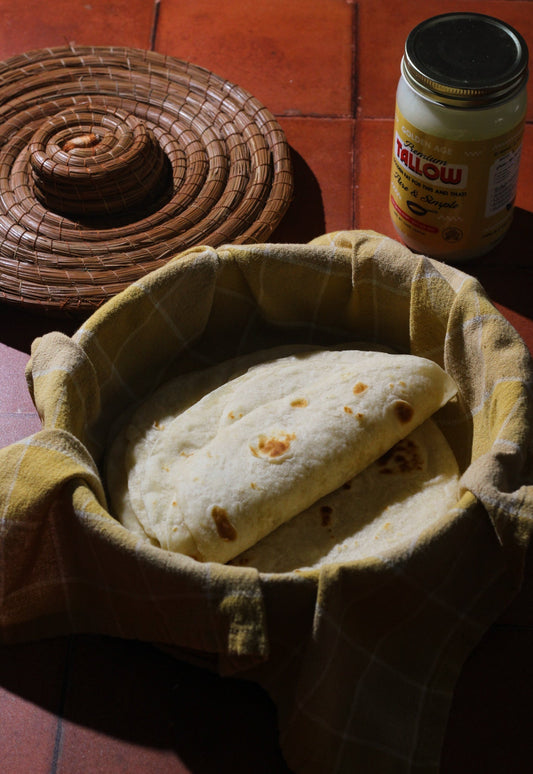 A stack of warm, hand-pressed Beef Tallow Tortillas in a wooden basket, showing golden-brown toasted spots.